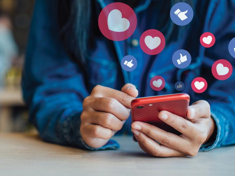 Photo illustration close-up of a person using a smart phone with a number of social media style likes and loves hovering over the phone.
