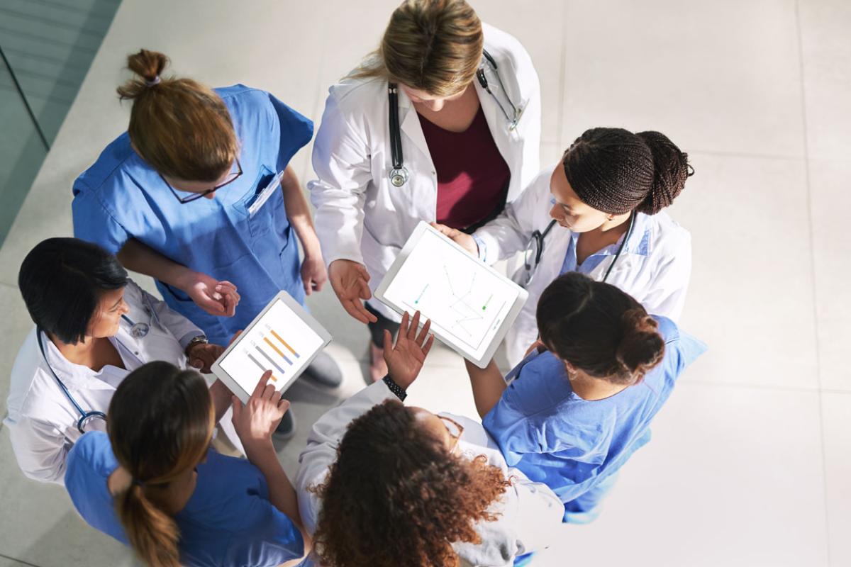 Seven physicians in a circle viewing two tablets