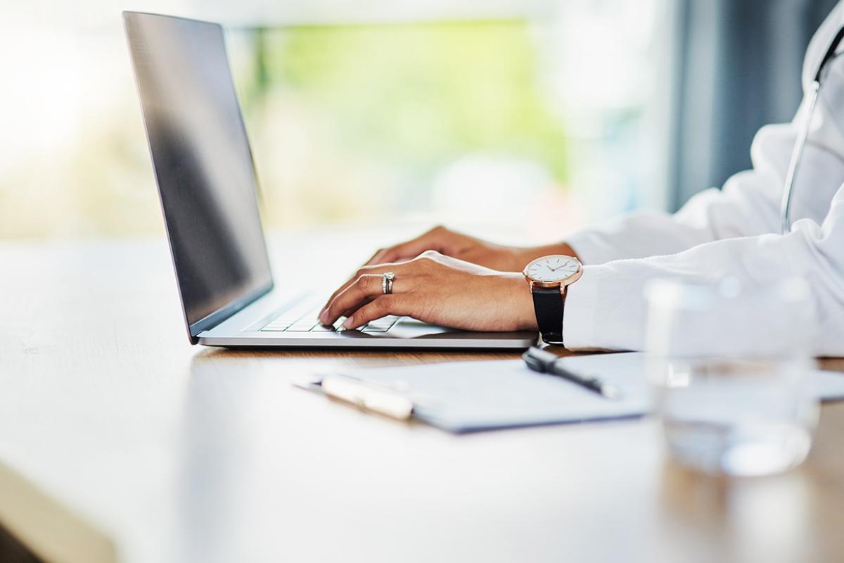 Tight shot showing physician's hands typing on keyboard.