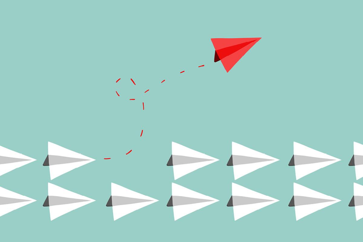 A red paper plane flying away from the pack of white paper planes