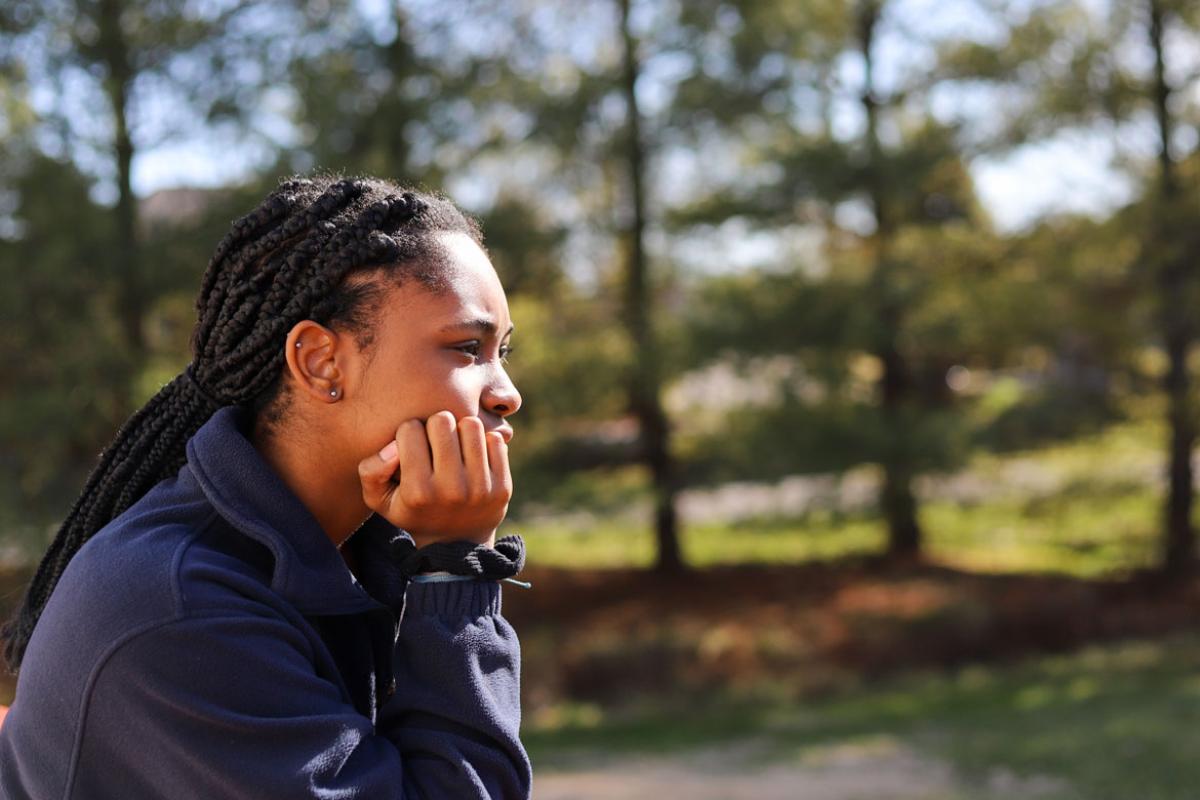Black woman sitting outside, looking in the distance