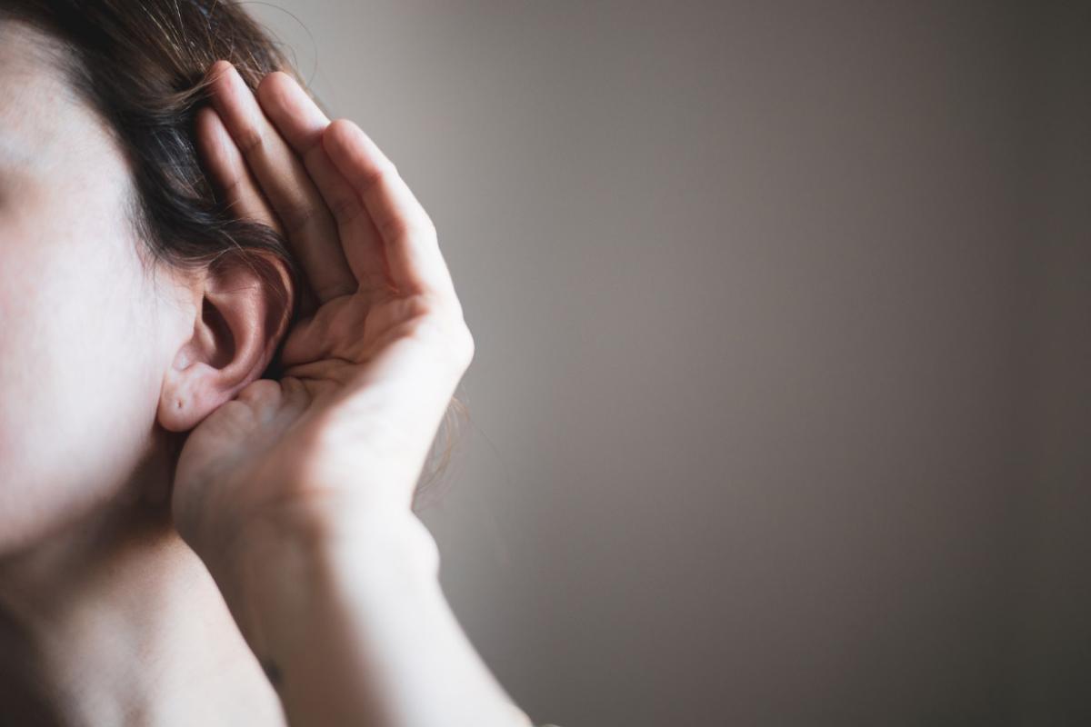 Extreme close-up of a person holding their hand to their ear, their face is cropped out.