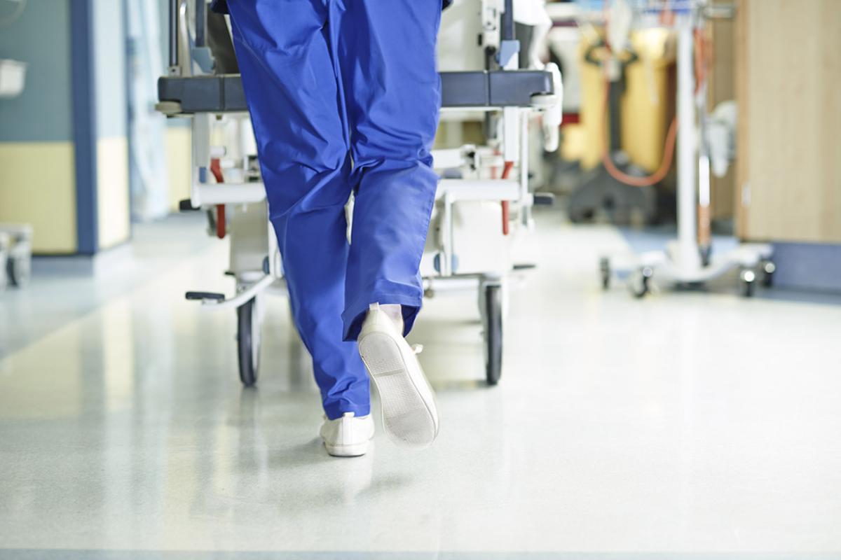 Tight shot of health care worker in scrubs pushing a gurney down a hospital hallway