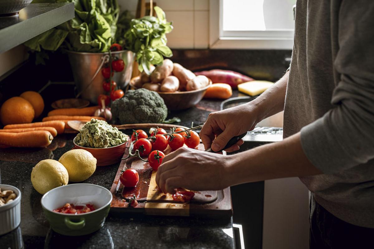 Human hands slicing tomatoes over a wooden table 
