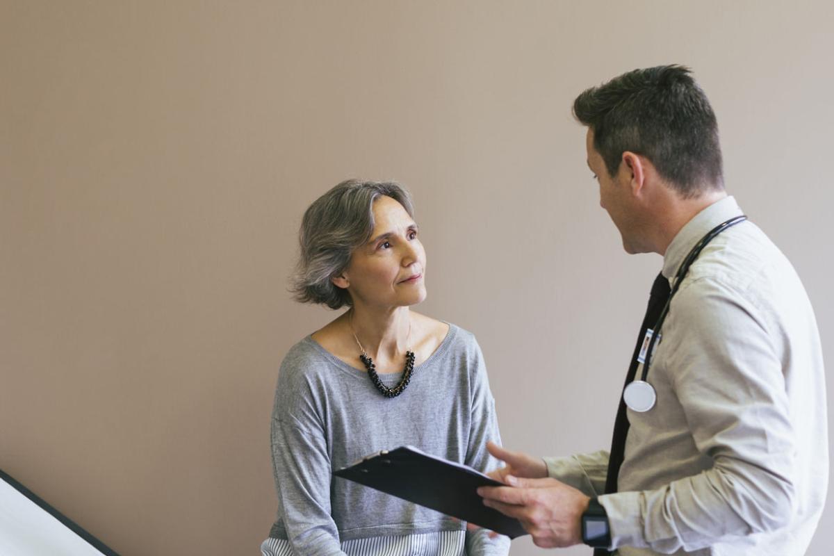Senior patient talking with doctor while sitting on bed against wall at hospital