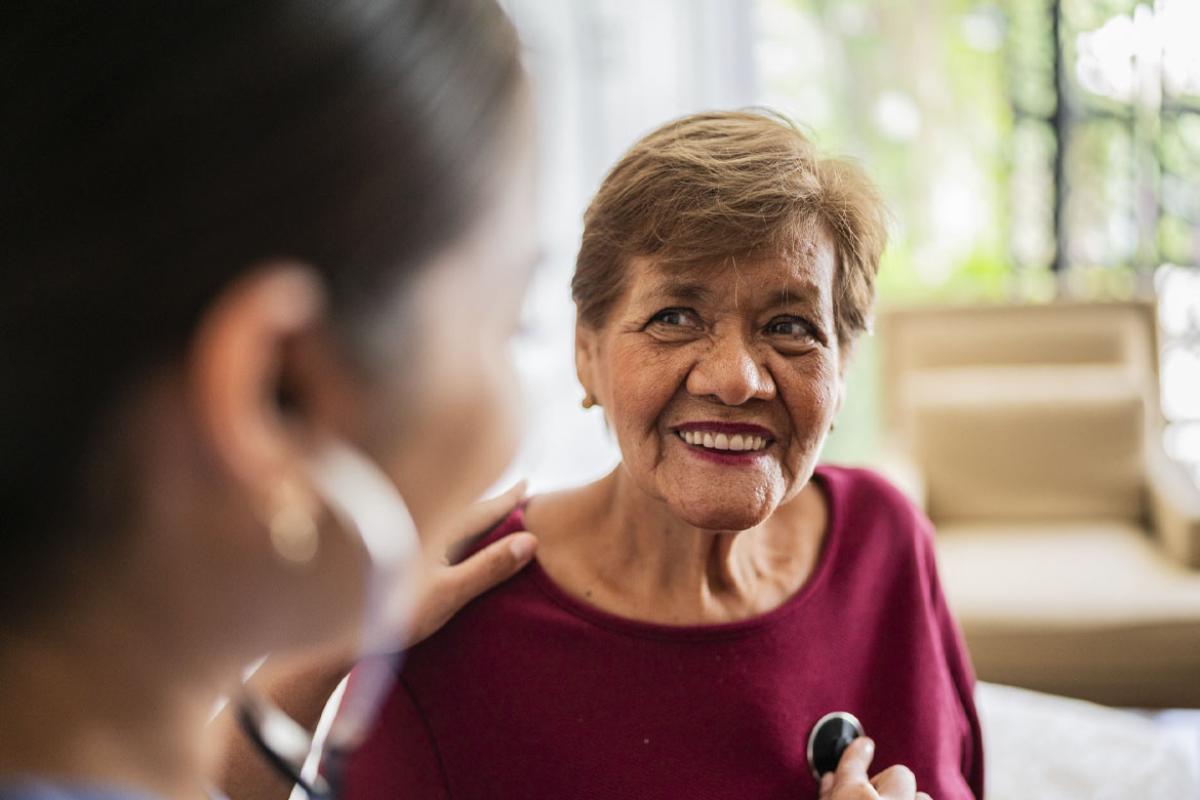 Home caregiver listening to a senior woman's heartbeat