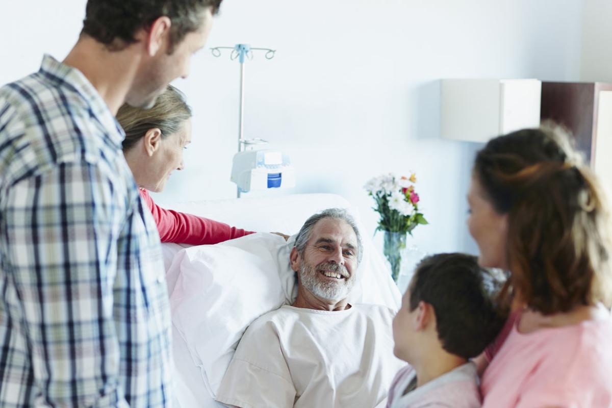 Multi-generation family visiting happy man in hospital bed