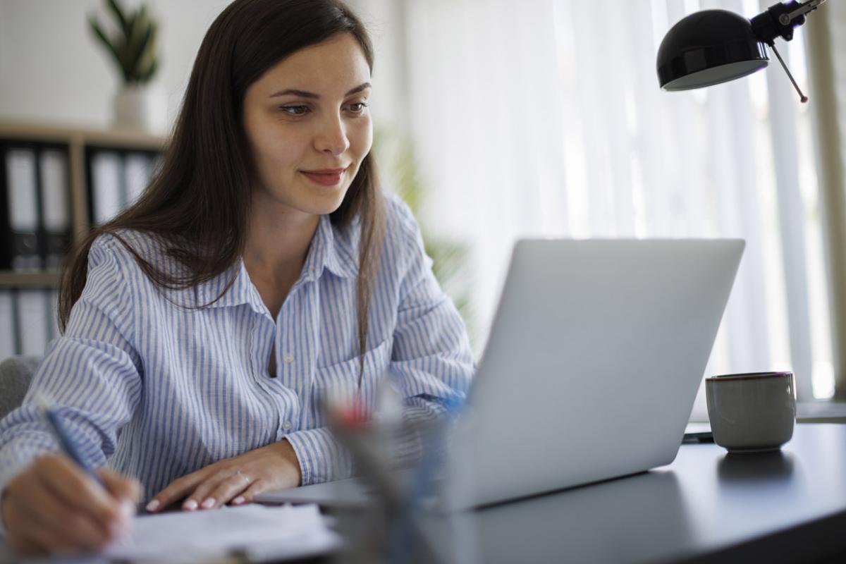 Person in front of a laptop while writing in a notebook