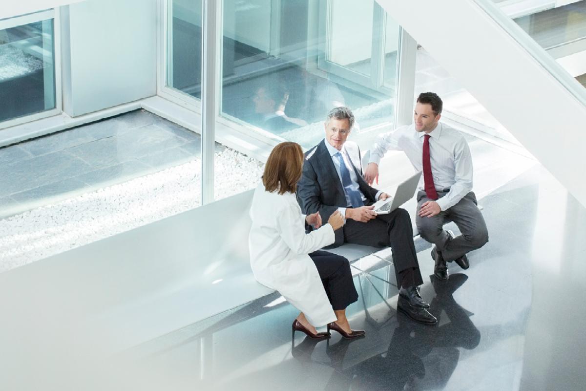 Two men sit on a bench and speak with a physician.