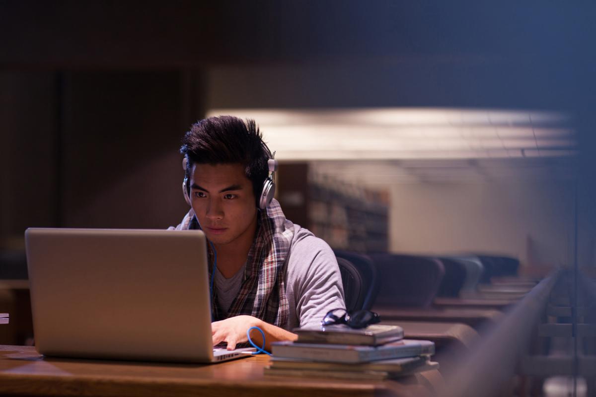 A man working on a laptop in a library with headphones on